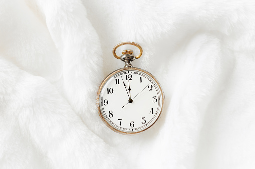Vintage pocket watch showing 12 oclock night, holiday midnight on clock face, twelve hour, Old shabby watch on white fur background, copy space. New Year, Christmas, xmas concept, minimal aesthetic