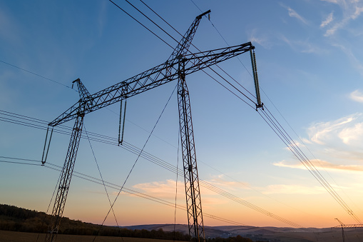 Dark silhouette of high voltage tower with electric power lines at sunrise. Transmission of electric energy concept.