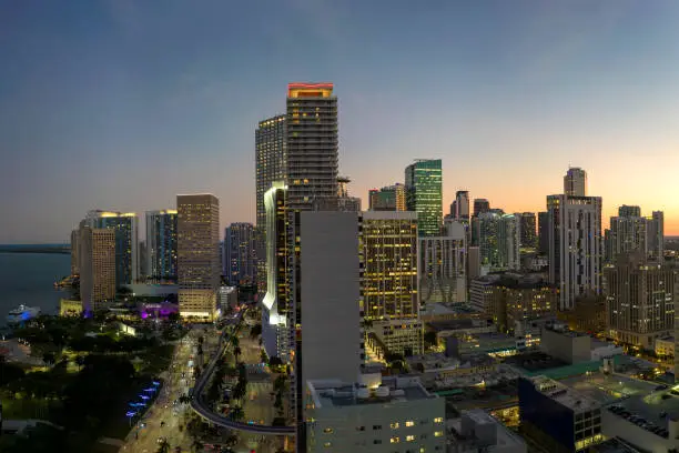Downtown district of Miami Brickell in Florida. Skyline with illuminated high skyscraper buildings and street with cars and Metrorail traffic in modern american megapolis.