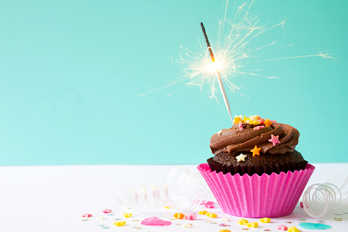 Chocolate buttercream cupcake with chocolate icing and a sparkler, on a blue background.
