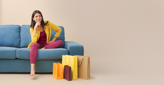 Happy woman sitting on the couch at home and many shopping bags, sales and shopping concept