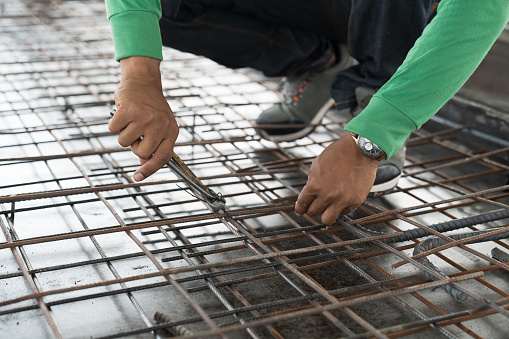 Hands of construction worker fabricating steel reinforcement bar at construction site. Male mason working with steel bar at work site
