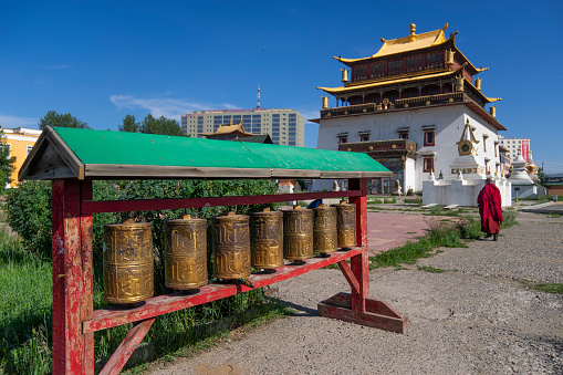 Ulaanbaatar, Mongolia - July 16, 2023: A monk walks past prayer wheels and a building near the Gandantegchinlen Monastery.