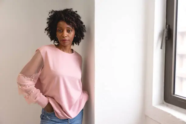 Black woman wearing a pink sweater near a window