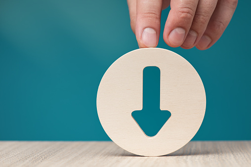 Arrow pointing down on a blue background. Banner with an arrow in a wooden circle in a hand close-up pointing down with copy space. High quality photo
