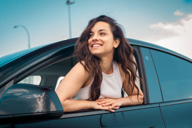 istock Smiling pretty lady sticking her head out the side view window while sitting in the car. Travel adventure drive, happy summer vacation concept 1665923575