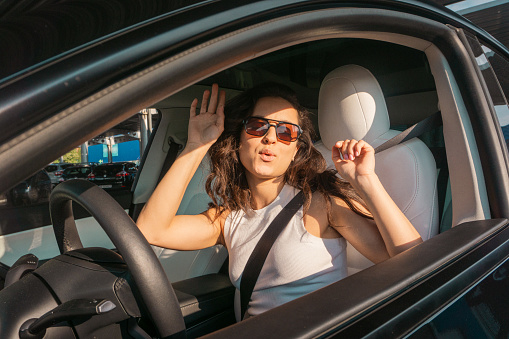 Happy pretty lady in sunglasses driving car on the road on sunny day while dancing the music. Travel adventure drive, happy summer vacation concept