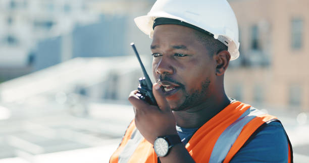 Communication, radio and engineering man for solar panels, renewable energy and urban city development. Technician, project manager or african person at outdoor building, grid check and walkie talkie stock photo