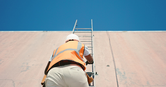Ladder, building and a man construction worker on site for engineering, maintenance or repairs from below. Industry, safety and an electrician, handyman or contractor climbing a wall for inspection