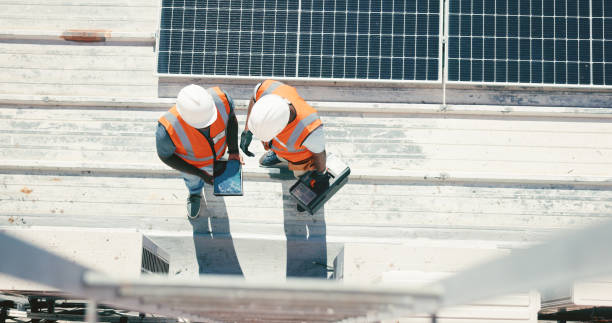 Renewable energy, solar panel and discussion, men on roof with tools at sustainable business in electricity. Planning, sustainability and photovoltaic power, engineer talking to technician from above stock photo