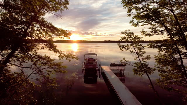 Flying toward docked pontoon boat at sunset on reflective lake