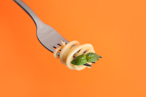 Fork with tasty pasta and basil on orange background, closeup