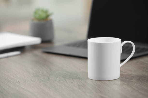 istock White ceramic mug and laptop on wooden table indoors. Space for text 1665957641