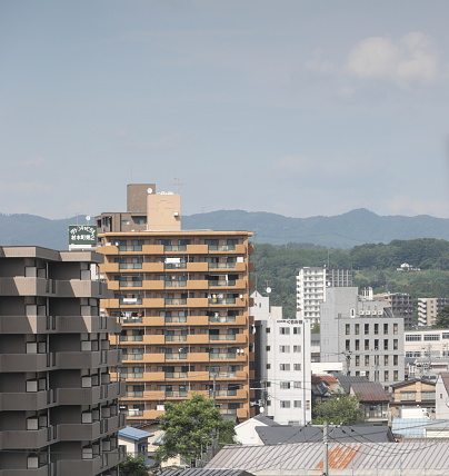 Morioka, Japan - June 10, 2023: Elevated view looking east to buildings in Morioka Ekimae Kitadori, the Morioka Station neighborhood near Kitakami River. Mountains stand in the background. Spring afternoon in Iwate Prefecture.
