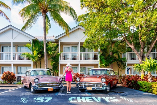 Key West, United States – September 04, 2023: A girl stands in front of two vintage cars in a resort driveway