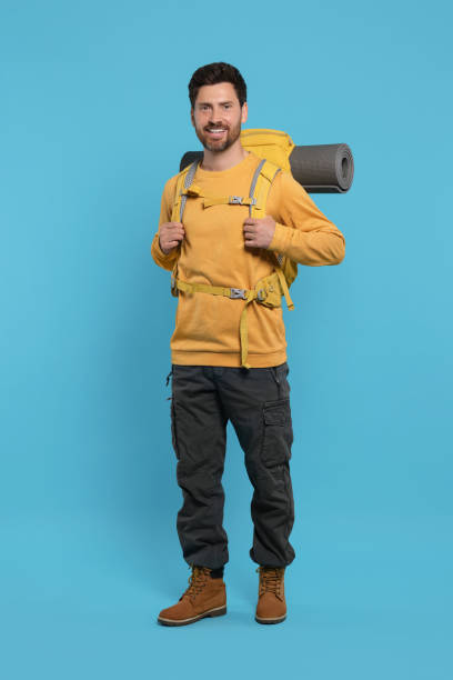 istock Happy man with backpack on light blue background. Active tourism 1666011371