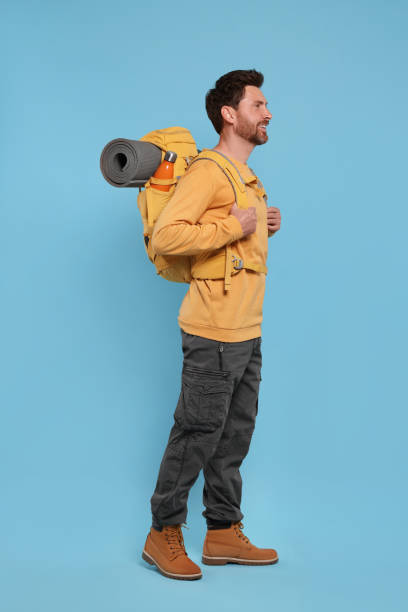 istock Happy man with backpack on light blue background. Active tourism 1666011391