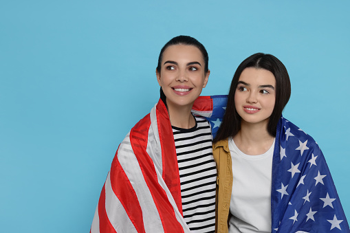 4th of July - Independence Day of USA. Happy woman and her daughter with American flag on light blue background, space for text