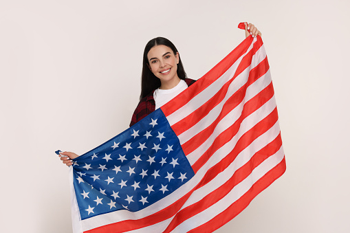 A beautiful young woman is posing for the camera with the American flag on her back. She appears to be proud and smiling for the camera.