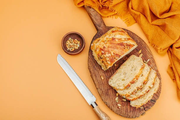 Fresh bread with pumpkin seeds. Home baking concept. Autumn decor, pumpkin, fall leaves. Wooden cutting board, pastel beige background, top view