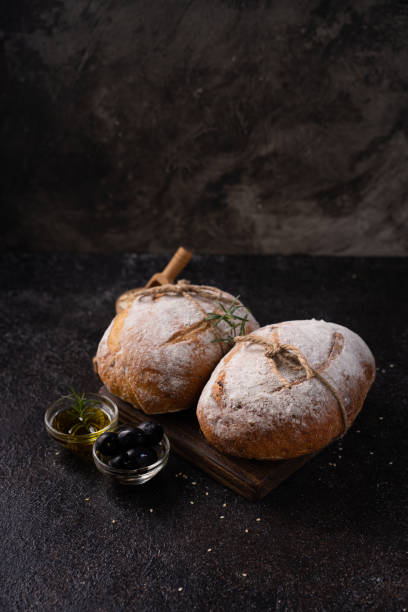 istock Freshly baked sourdough ciabatta bread with olives and rosemary on a black rustic table. Artisan bread 1666070176