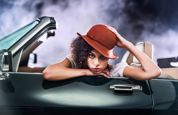 Fashionable Retro African-American young woman is sitting in old timer car and looking at camera.