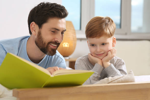 istock Father reading book with his child on bed at home 1666097095
