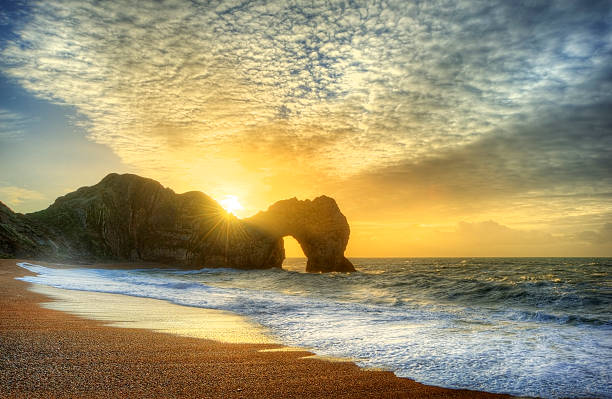 яркий восход солнца над океан с рок-труба на переднем плане - durdle door стоковые фото и изображения