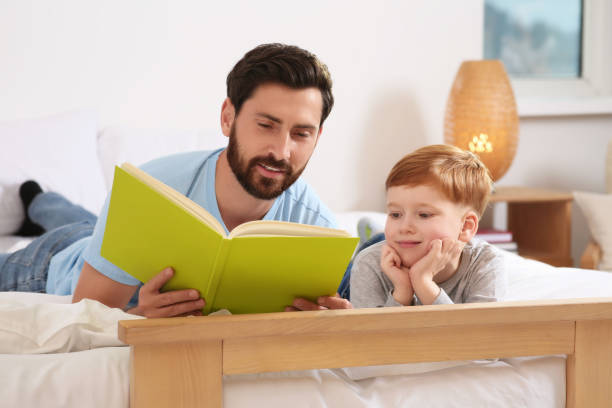 istock Father reading book with his child on bed at home 1666097717