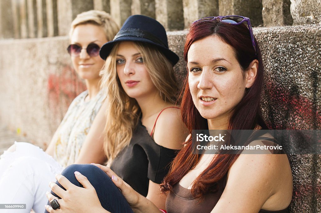 Three pretty young hipster girls Three pretty young hipster girls sitting against the wall Adult Stock Photo