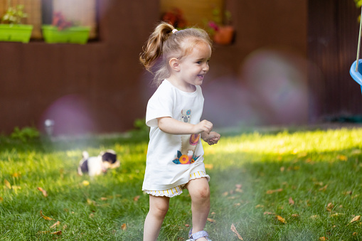The simple pleasures of childhood - a girl running in a lush, green yard, playing with puppy.