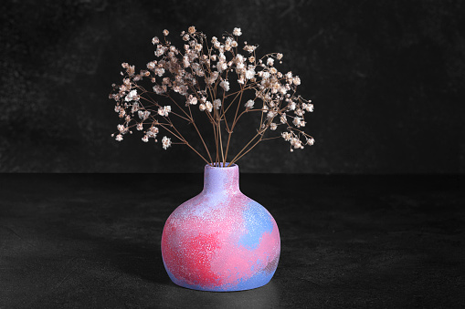 Gypsum multicolored vase with a bouquet of dried flowers on a black background, front view, copy space, low key. Home decor.