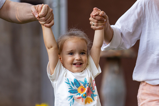 A heartwarming scene of parents playfully engaging with their young daughter, lifting her hands in the air.