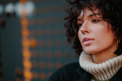 Side view shot of a beautiful dark haired curly girl standing against the wall with holes and looking into the distance. Focus on her pretty face with slightly open lips and dark eyes. Copy space.