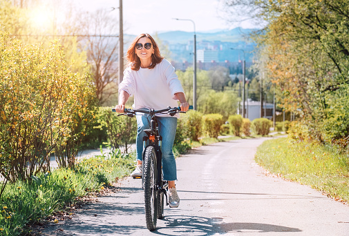 A happy smiling Caucasian woman in fancy sunglasses riding a bicycle on the city park street. Ecology sustainable transport and happy people concept image.