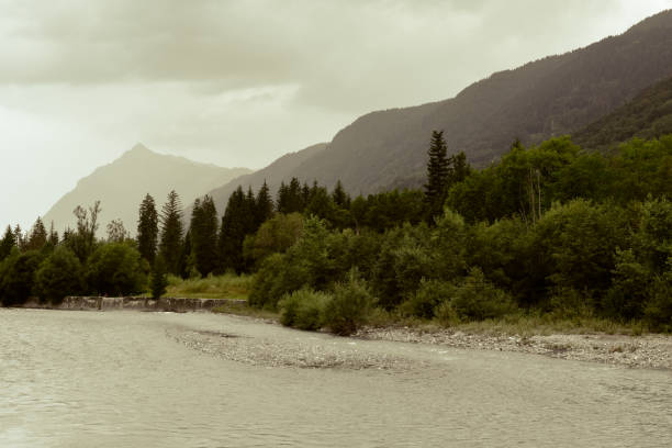 River flowing through a mountain valley landscape with misty clouds over the mountain peaks