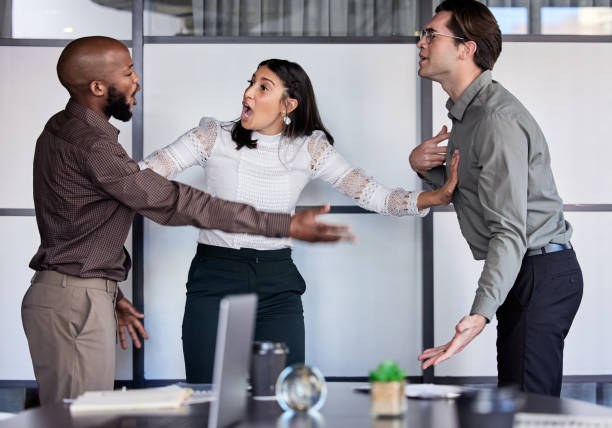 tiro de uma jovem empresária tentando impedir seus dois colegas de brigar em um escritório - businesswoman frustration rudeness business - fotografias e filmes do acervo