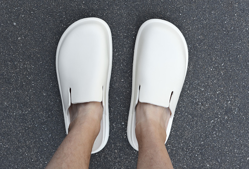 Closeup of a man's feet in new plastic clog sandals on pavement.