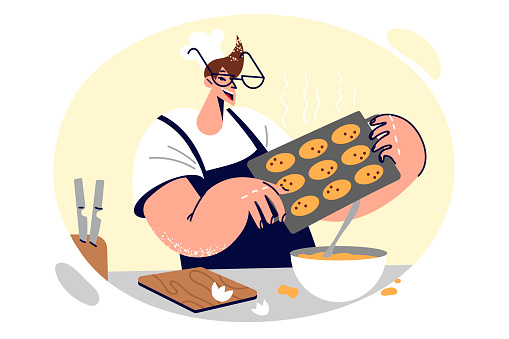 Man cook works in confectionery shop and holds tray with oatmeal cookies prepared by own hands. Cheerful chef learning how to cook delicious desserts, standing in kitchen of restaurant or cafe