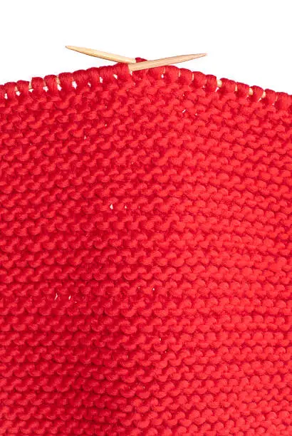 Hand-knitted work of a very thick red wool yarn with two knitting-needles on white background.