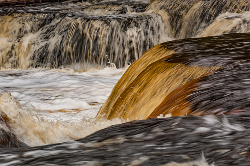 Lower Tahquamenon Falls, Tahquamenon Falls State Park, near Paradise, Michigan, amber color of the water is caused by tannin leached from trees. Autumn colors in the trees. Tahquamenon River. Very colorful water color.