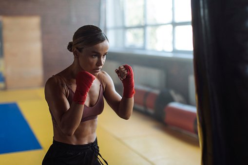 In her boxing training session, a fit young woman delivers punches to a punching bag