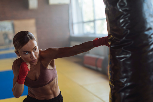 During her boxing session, a fit young woman works on her punches by hitting a bag