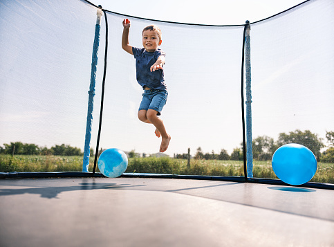 little sports girl jumps on a trampoline. Outdoor shot of girl jumping on trampoline, enjoys jumping in home. happy summer vacation.