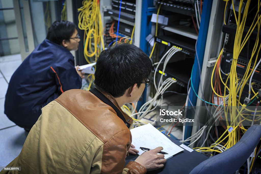 Dois administradores de rede estão trabalhando na sala do servidor - Foto de stock de Cabo de conexão de rede royalty-free