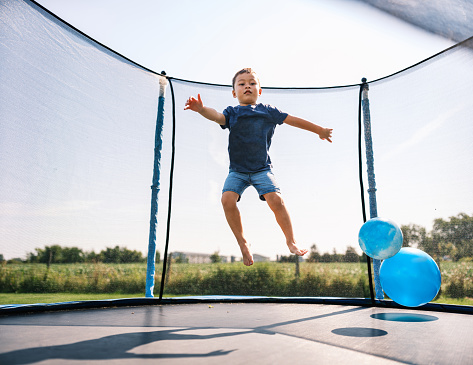 Full length low angle portrait of happy African-American boy jumping on trampoline in colorful kids play center, copy space