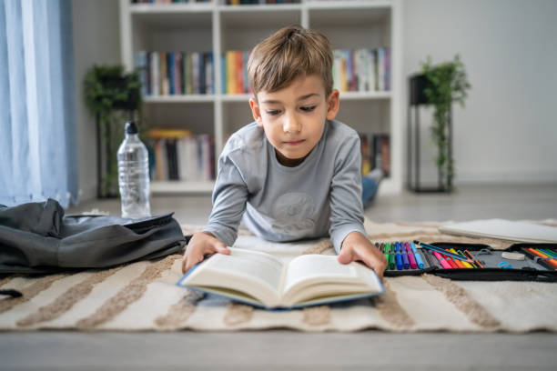istock caucasian boy pupil student read book at home on the floor study learn 1666408921