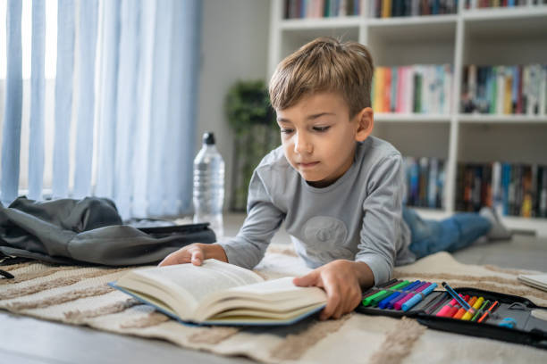 istock caucasian boy pupil student read book at home on the floor study learn 1666410043