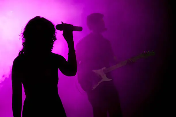 Female singer and guitarist silhouette on violet background.