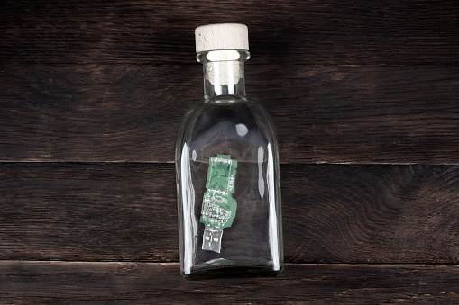 USB memory stick as letter in vintage bottle on wooden deck
